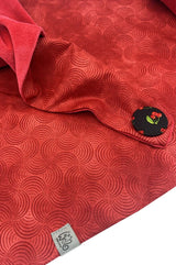 Detailaufnahme eines roten Dreieckstuchs mit dekorativem Wellenmuster und schwarzem Knopf mit kleinem Kirschmotiv als besonderem Akzent.
