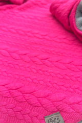 Pinkes Strick-Dreieckstuch in Texturdetailansicht, weiches Material und grauer Knopf.