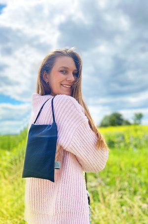 junge frau trägt kleine schultertasche für handy und krimskram dunkelblau mit softschnur