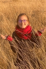 junge frau mit rotem tuch und bordeauxroten stulpen sitzt in der wiese spätsommerstimmung